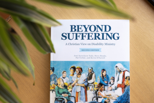 Book cover of "Beyond Suffering, Second Edition," featuring an illustration of the Luke 14 banquet, with Jesus standing at a table surrounded by people with disabilities.