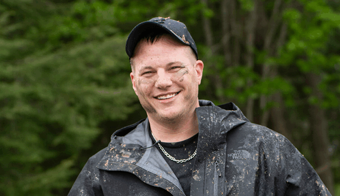 Mark Stallion smiles happily for the camera, his face and body covered in mud as he rides an all-terrain vehicle.