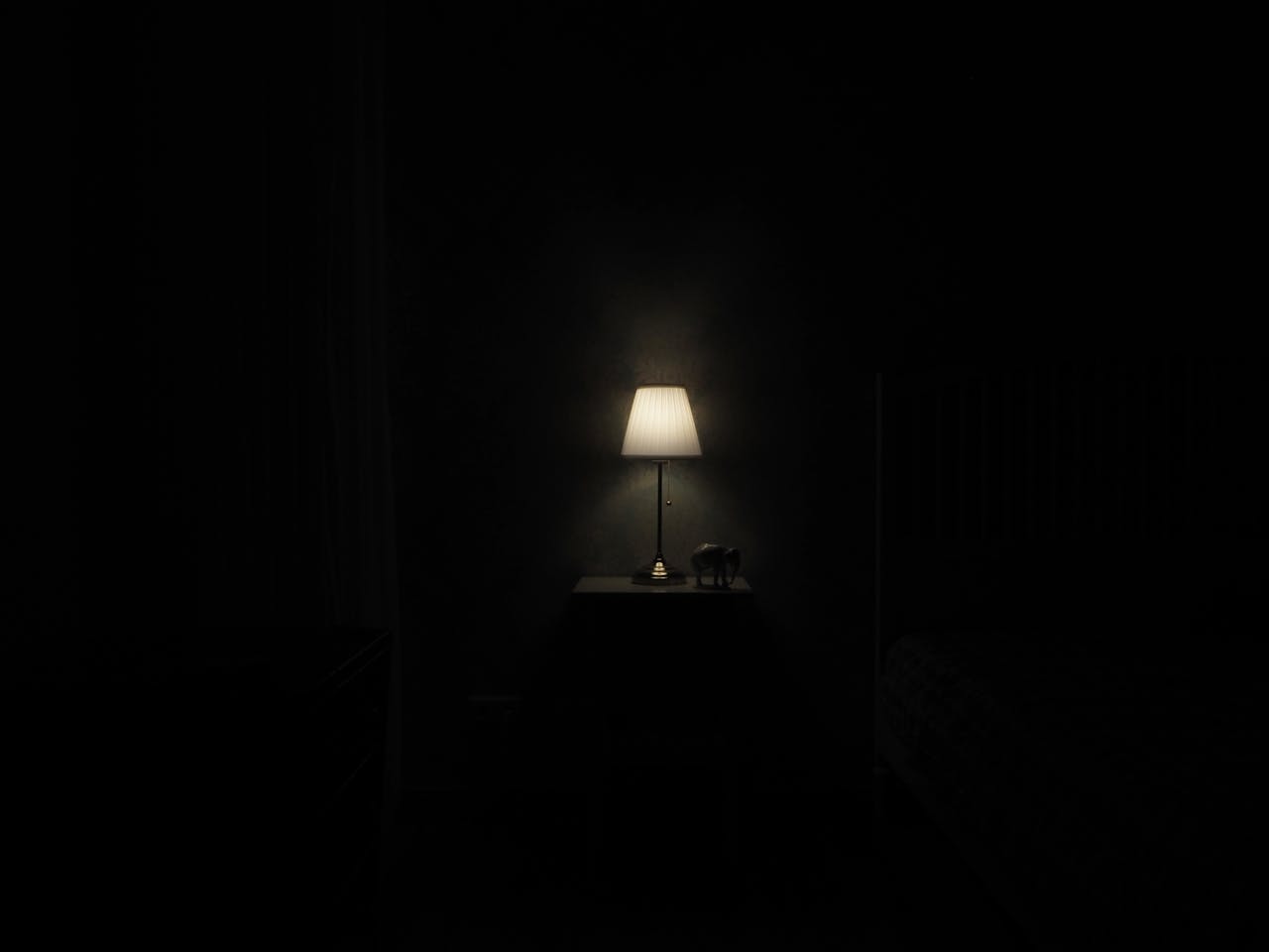A lamp on a side table glowing in a dark room.