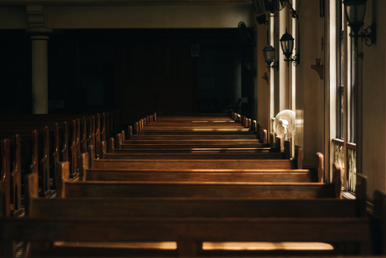 Empty wooden church benches illuminated by sunlight streaming through a window.