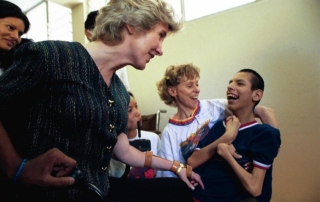 Joni Eareckson Tada smiling at a boy with a disability; both are smiling at each other, with two other women in the background.