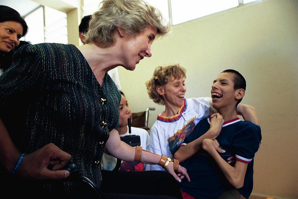 Joni Eareckson Tada smiling at a boy with a disability; both are smiling at each other, with two other women in the background.
