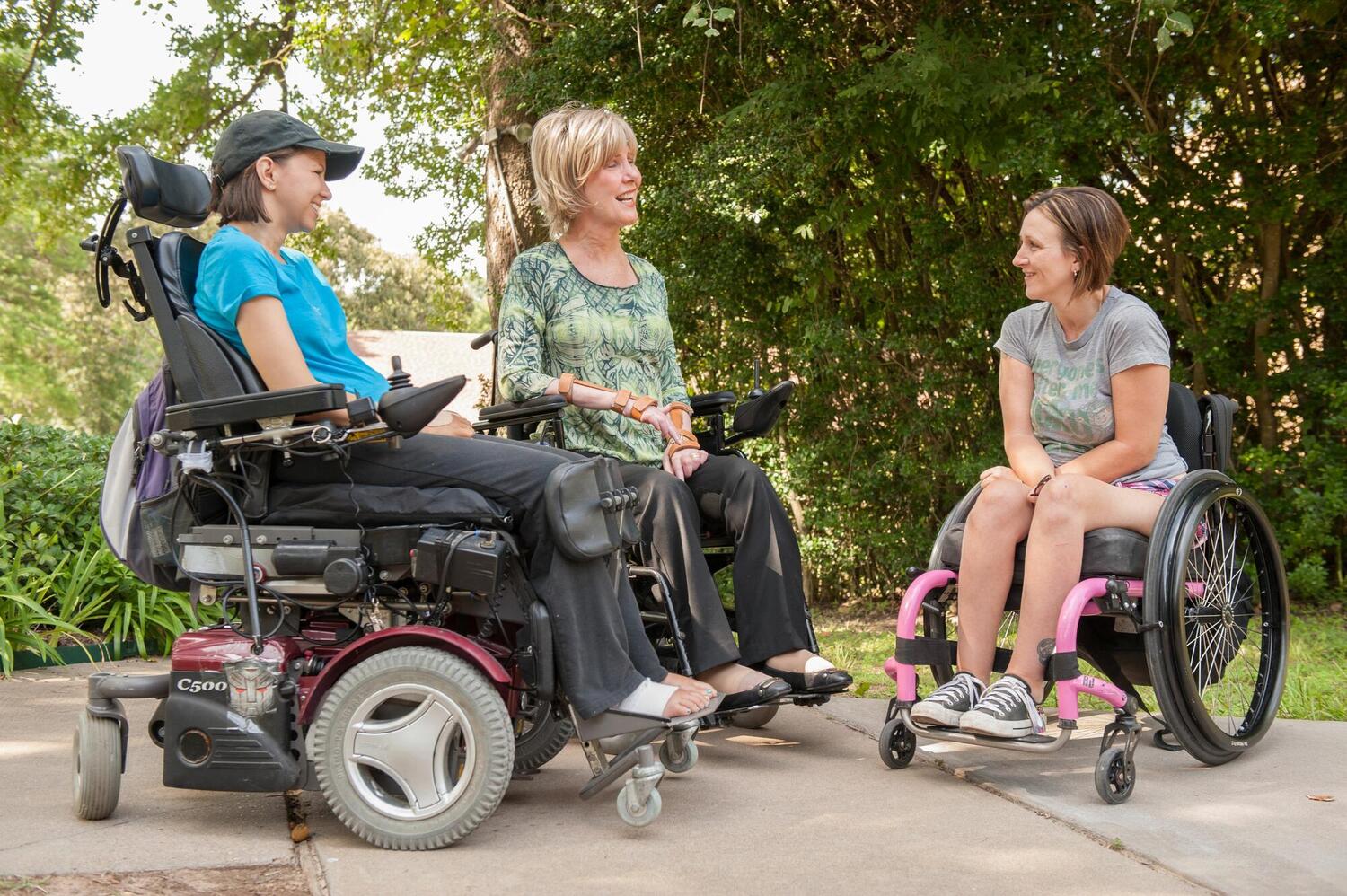 Joni Eareckson Tada speaking with two other women who are in wheelchairs; all three are smiling and looking at each other as they talk.