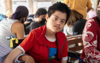 Donovan sitting in his new wheelchair with people in the background.