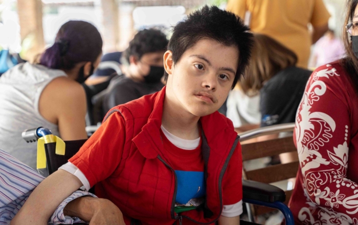 Donovan sitting in his new wheelchair with people in the background.