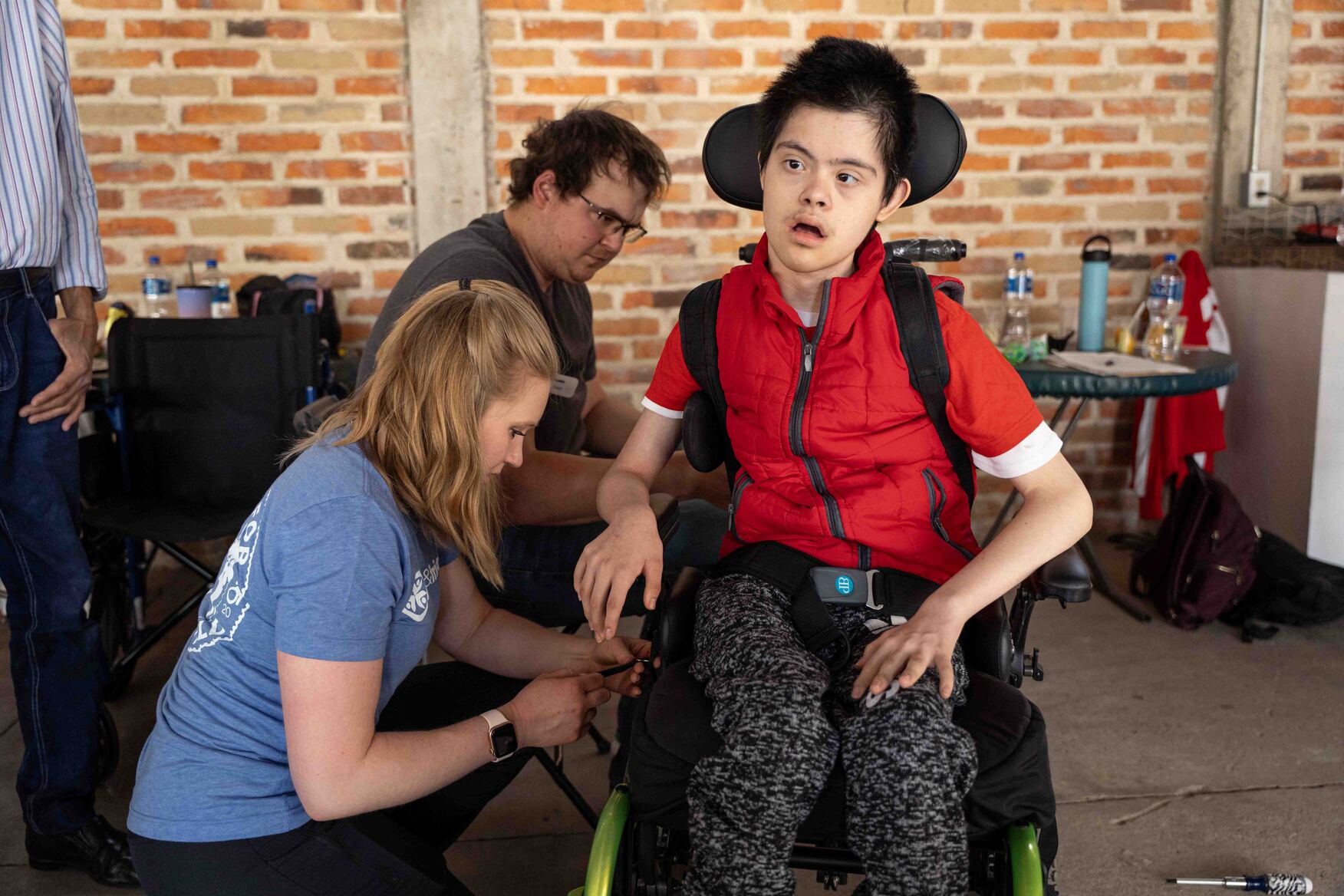 Donovan sitting in his new wheelchair as two Joni and Friends volunteers adjust it.