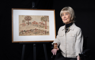 Joni Eareckson Tada next to her artwork titled "Steeplechase," which depicts three horses, each with a rider, jumping over hurdles.