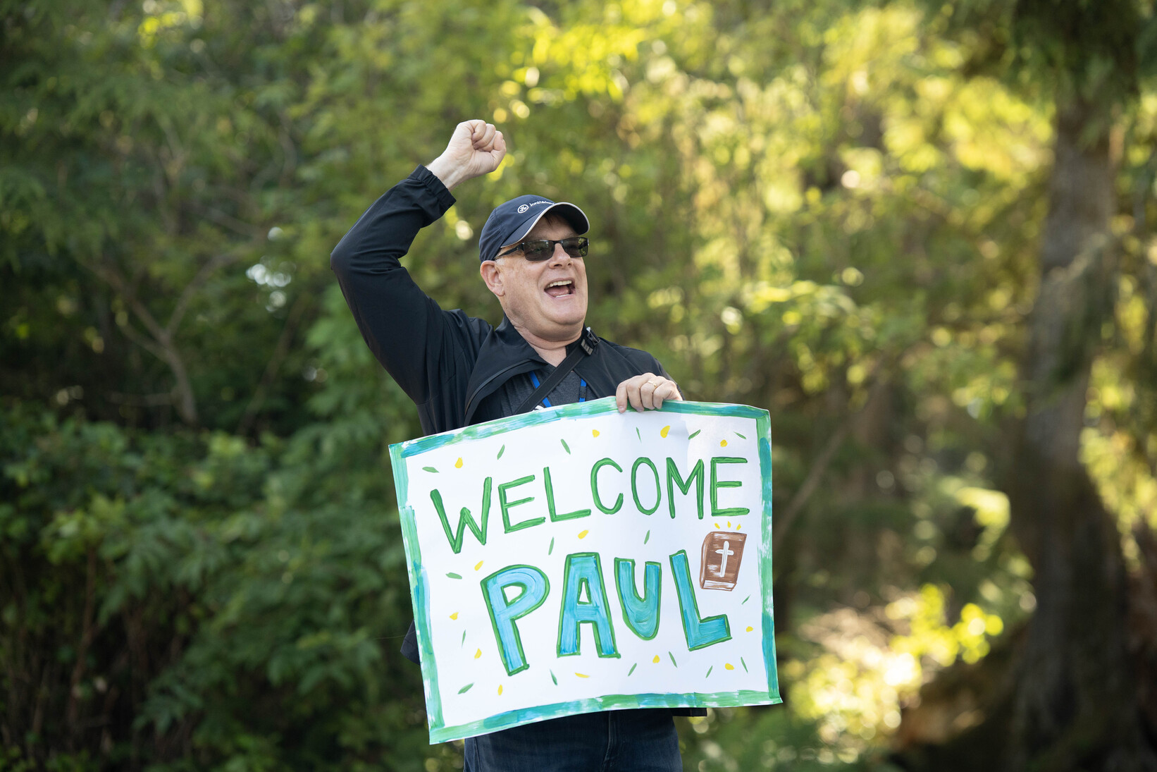 Shawn yelling while holding a banner that says "Welcome Paul" with a Bible graphic drawing.