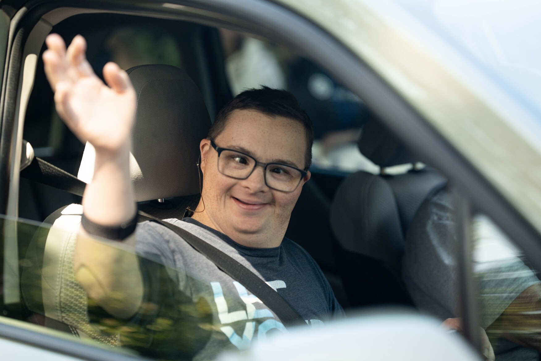 Paul seated in the passenger’s seat, waving with the car window open.