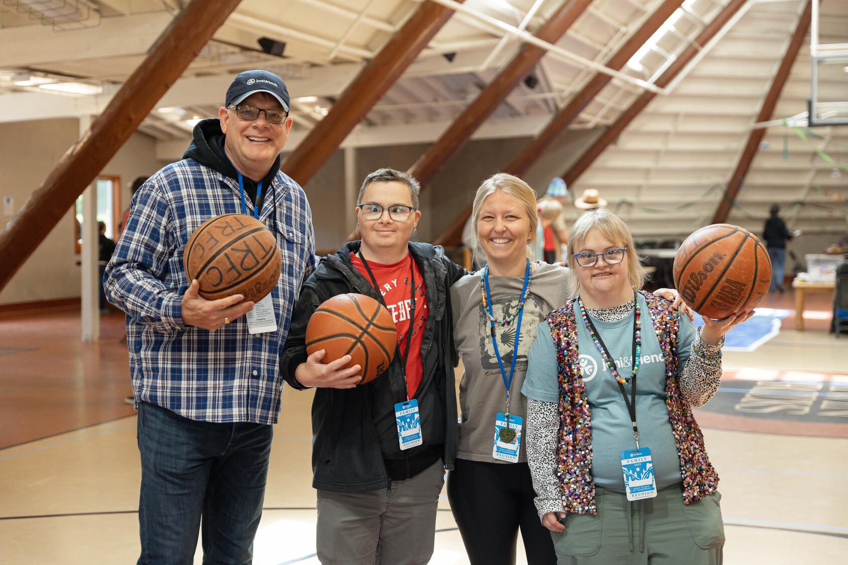 Shawn, Paul, and Emily holding basketballs in each hand, standing next to Katie, all smiling and posing for the camera on a basketball court.