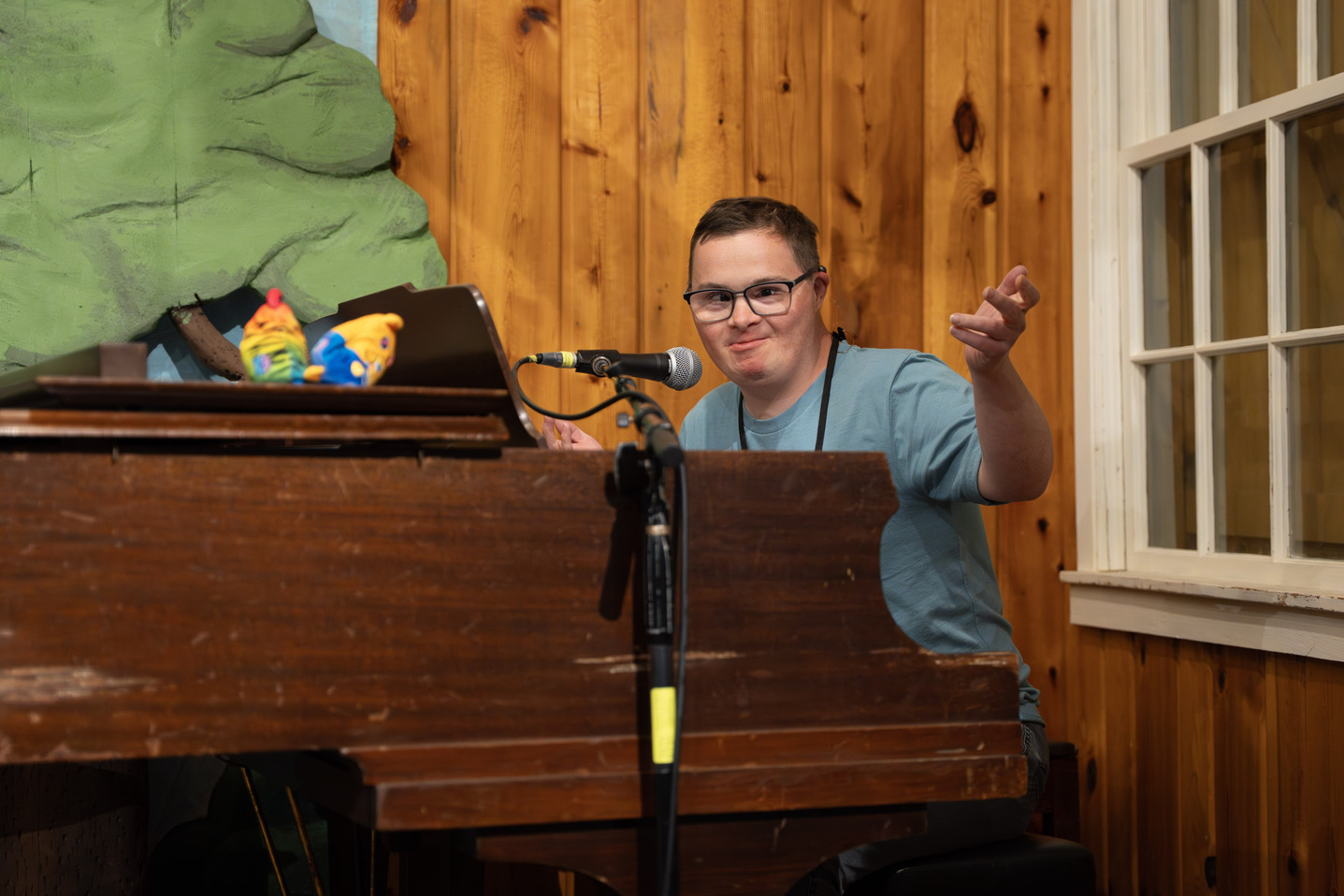 Paul, a man with Down syndrome, sitting in front of a wooden piano and a microphone.