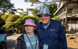 Paul, a man with Down syndrome, and Shawn wearing colorful bucket hats, smiling at the camera.