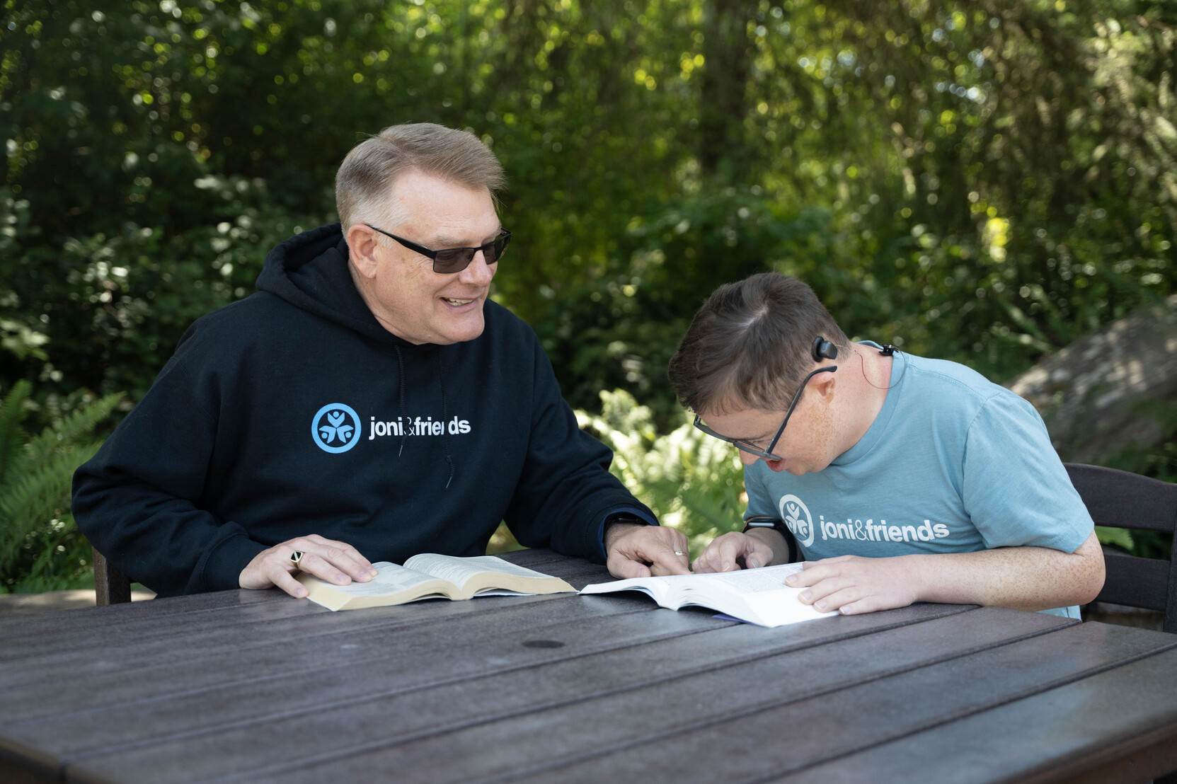 Shawn and Paul reading the Bible side by side, with open Bibles in front of them. Shawn points to a scripture while Paul looks on carefully and engaged.