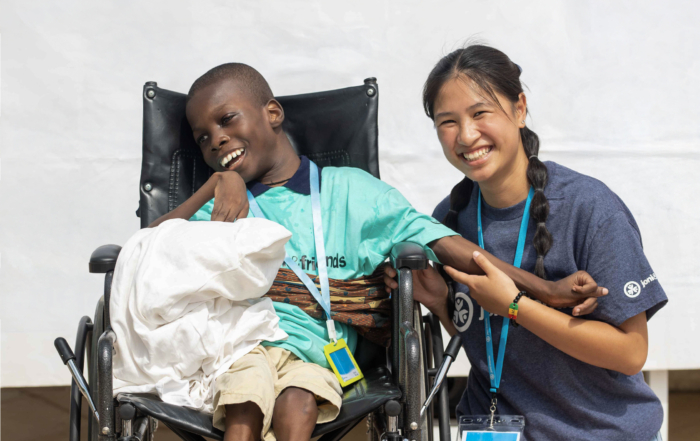 Kofi sitting in his wheelchair, smiling widely next to Ailah, a Joni and Friends intern