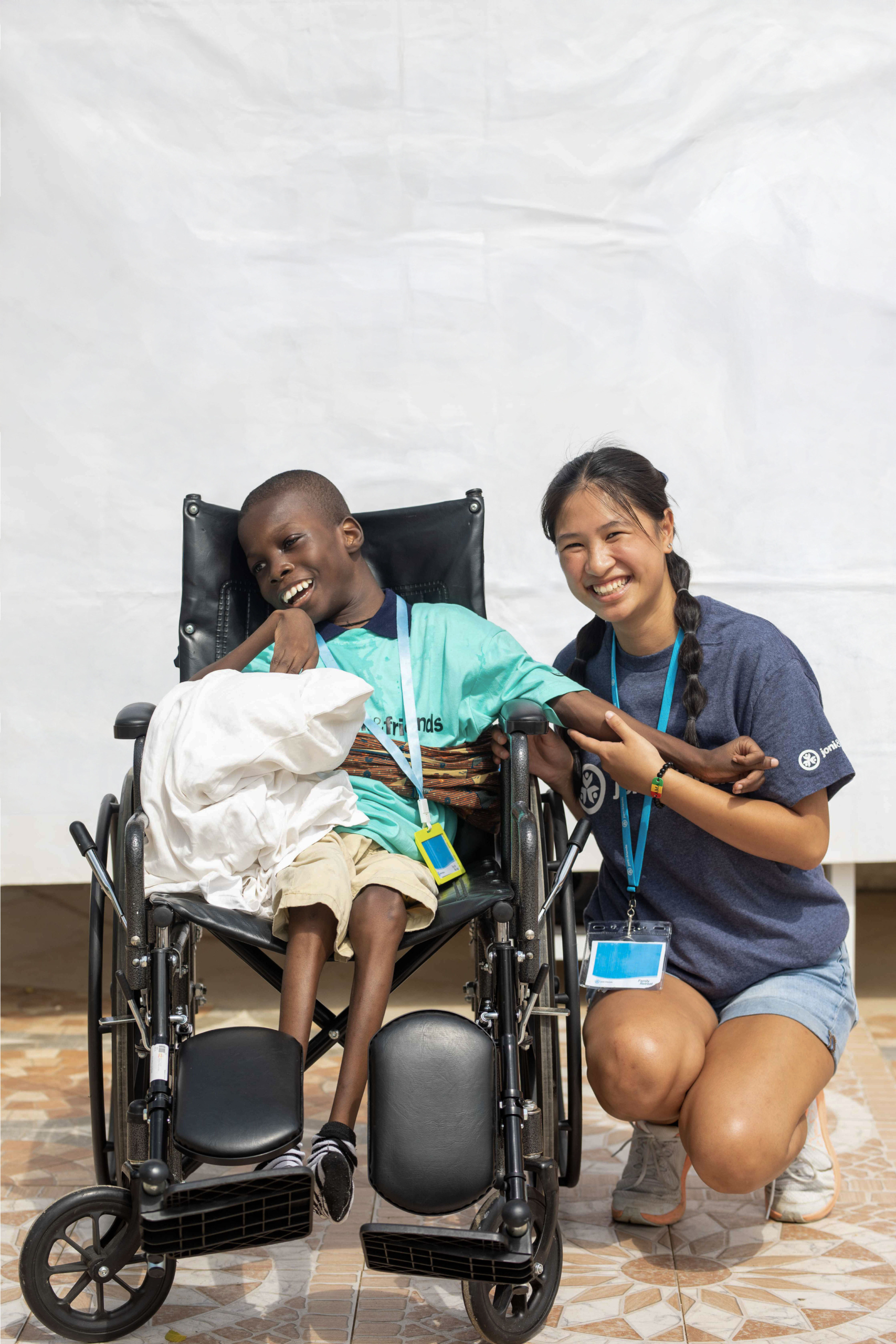 Kofi sitting in his wheelchair, smiling widely next to Ailah, a Joni and Friends intern
