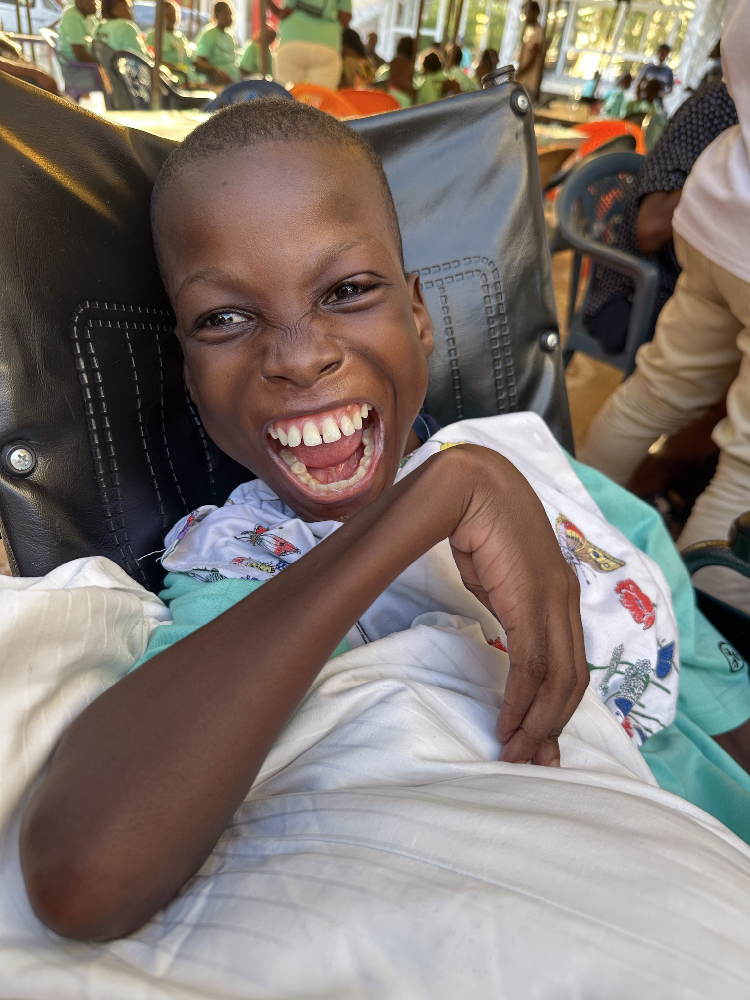 Kofi with his widest smile looking so happy and excited sitting on his wheelchair