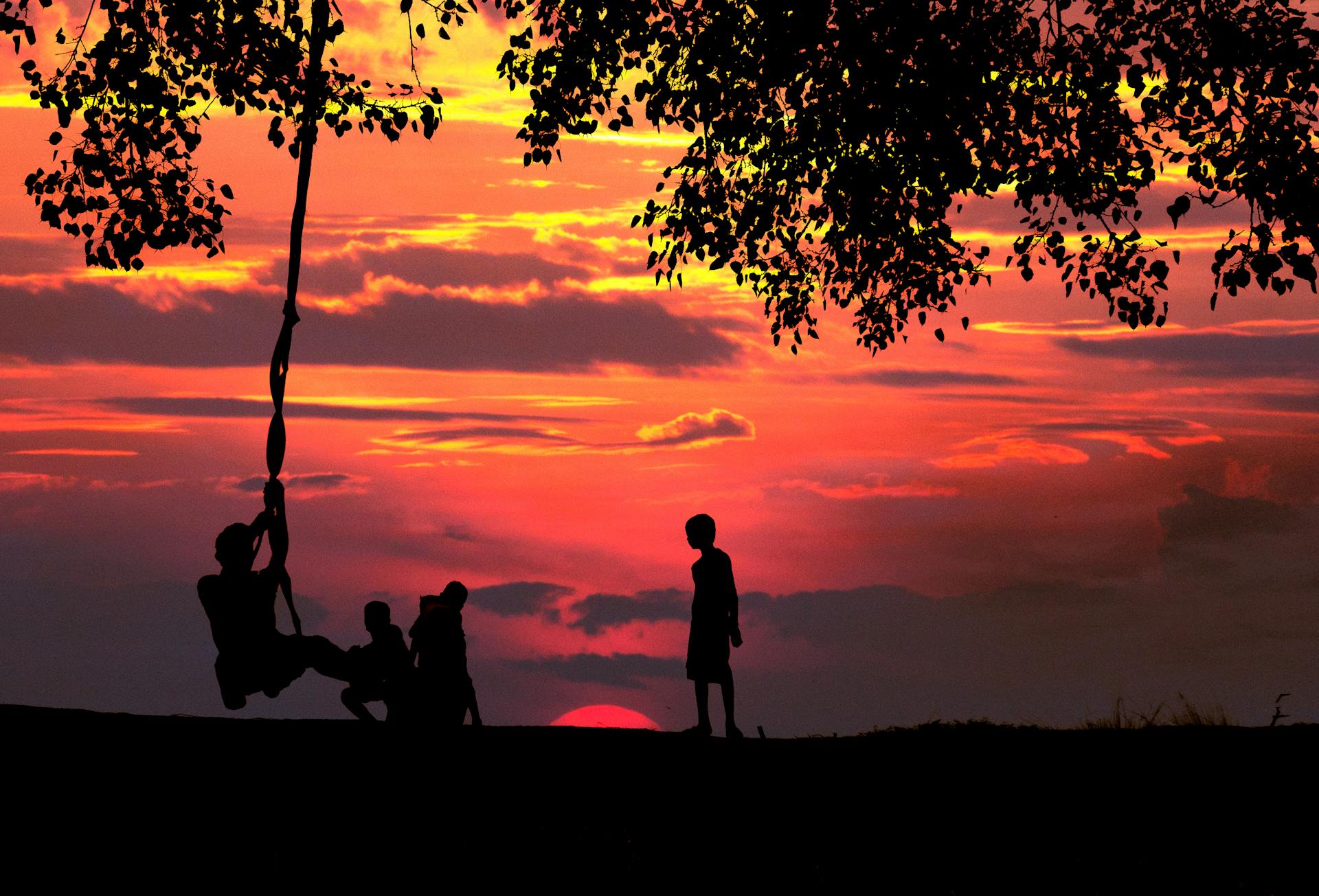 Silhouettes of people having fun together during a vibrant sunset, with the sky glowing in warm orange and pink hues.