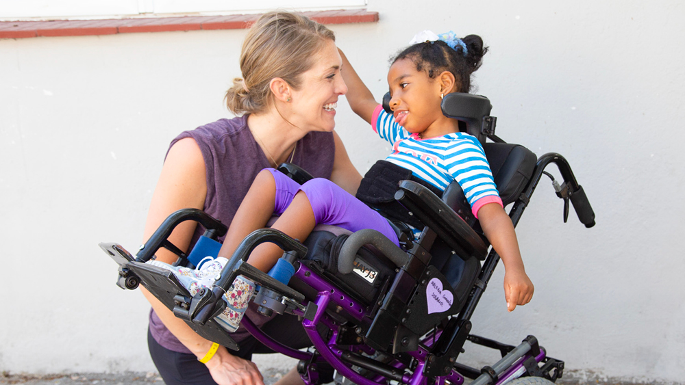 A volunteer smiles at a girl in her new pediatric wheelchair