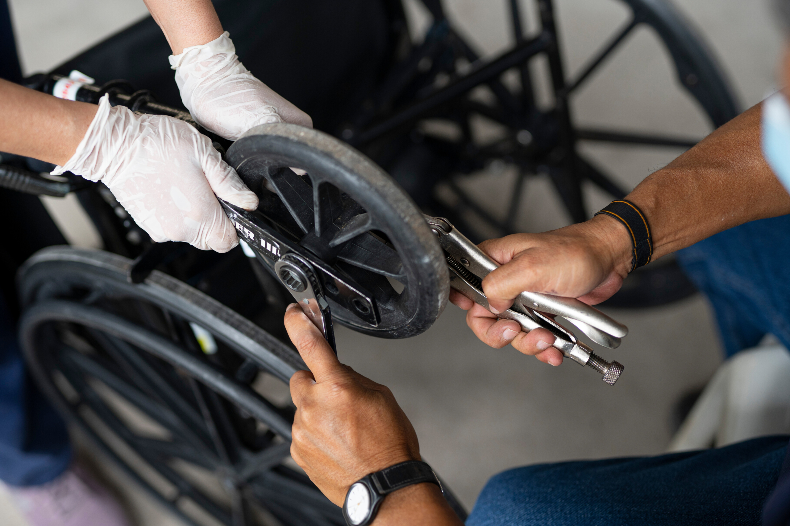 Close-up of hands fixing the wheel of a wheelchair with a wrench.