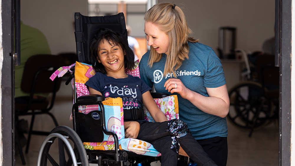 A girl smiles in her new wheelchair as a volunteer smiles at her