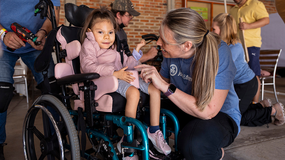 A girl smiling in her new wheelchair as an intern smiles at her