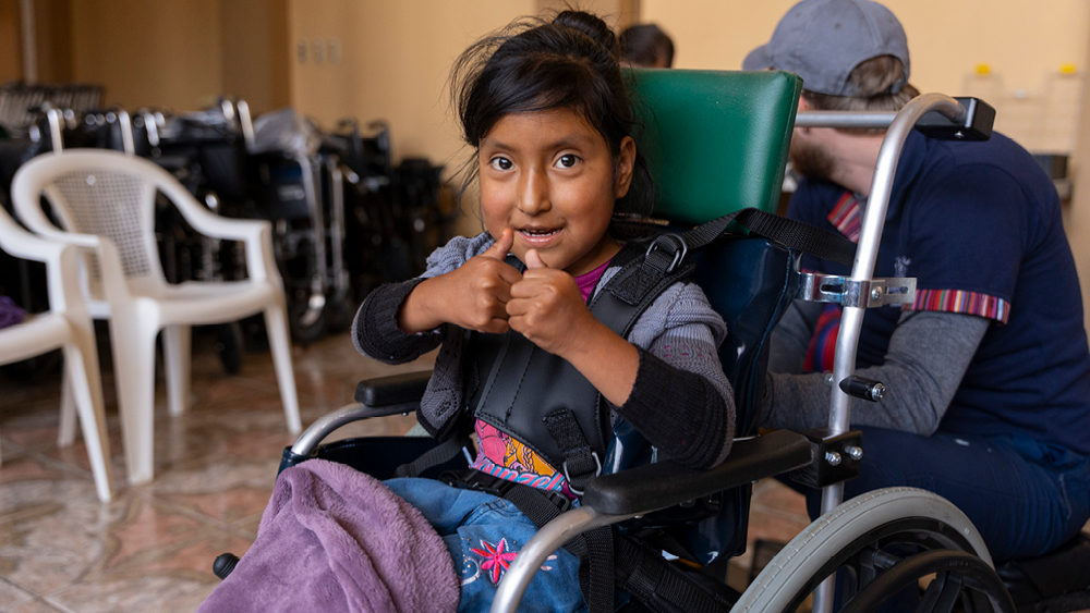 A young girl in her wheelchair gives a thumbs-up to the photographer