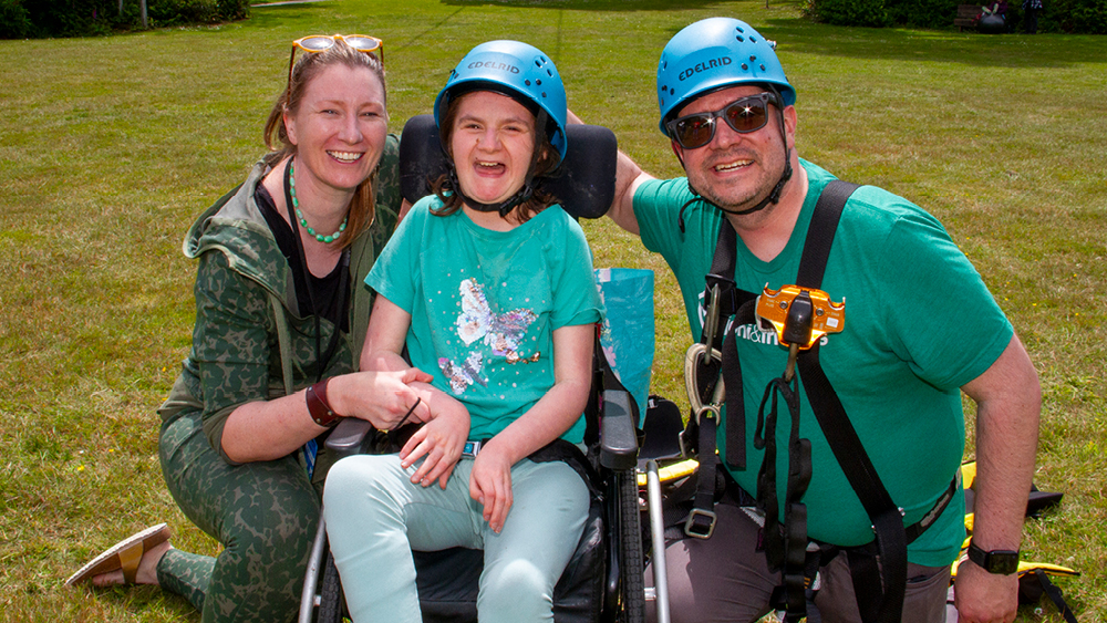 25_FR_Oregon_WK1_0252_1000x563 A girl in a wheelchair next to her mom and dad. All are smiling for the camera.