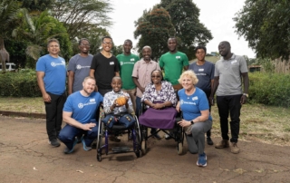 Melvin, sitting in his new sports wheelchair, holds a basketball. His mom, Ruth, sits beside him in her new wheelchair. Volunteers from Joni and Friends surround them, all smiling happily for the camera.