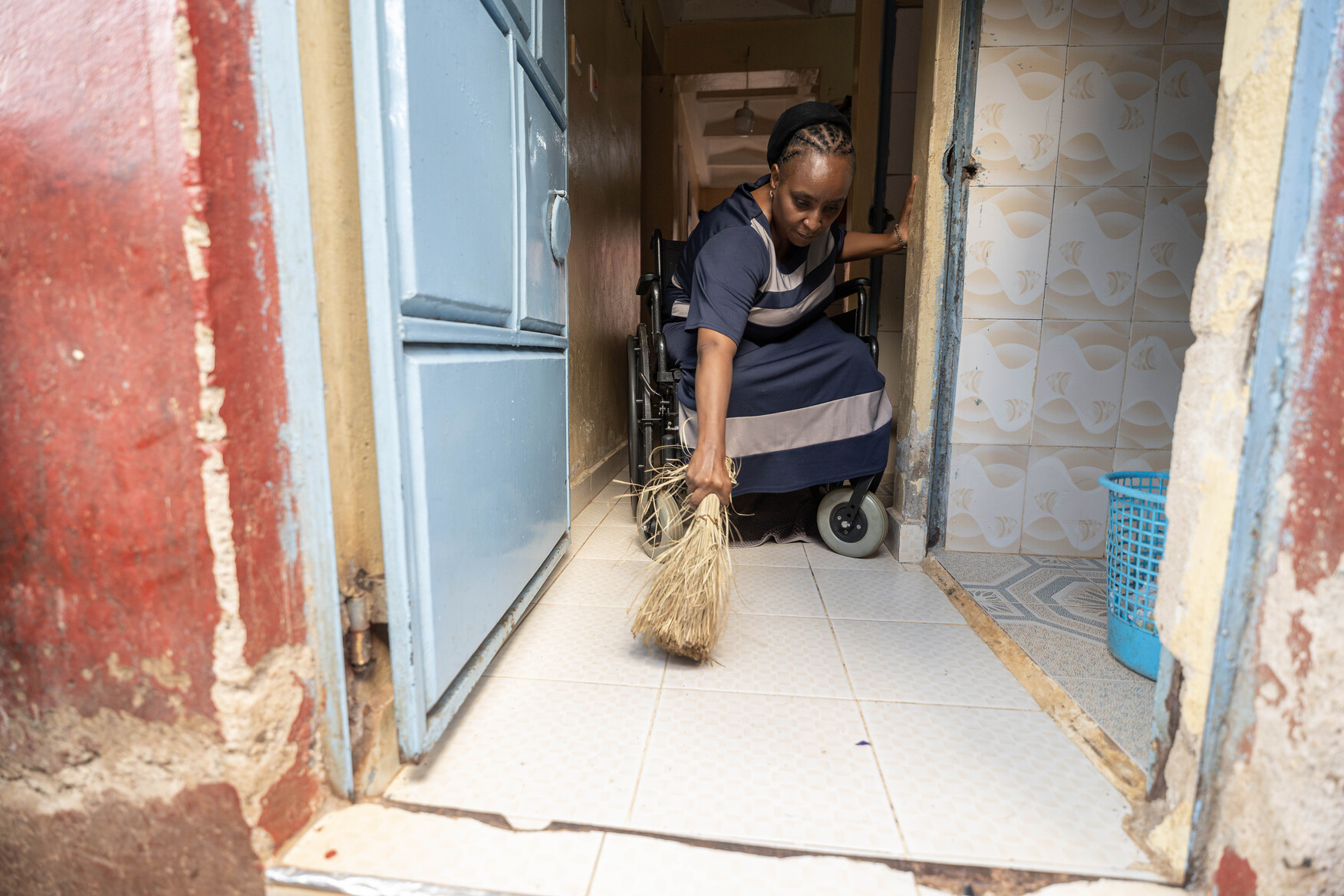 Ruth, in her new wheelchair, is sweeping the floor with a broom.