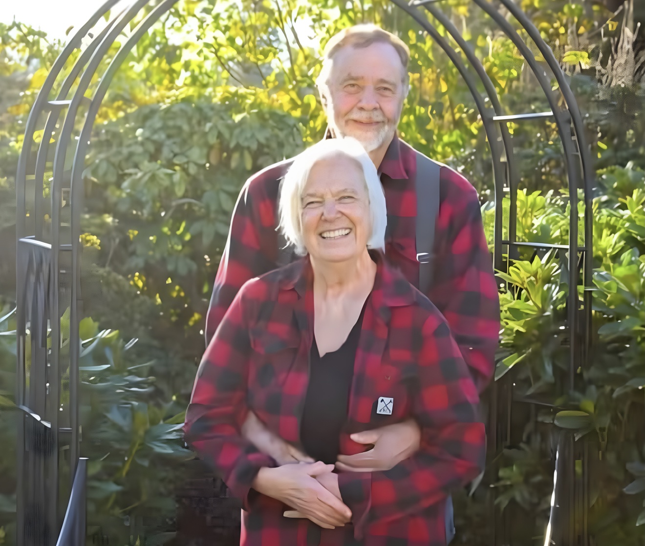 Jeanne with her husband hugging her from behind. Both are smiling for the camera.