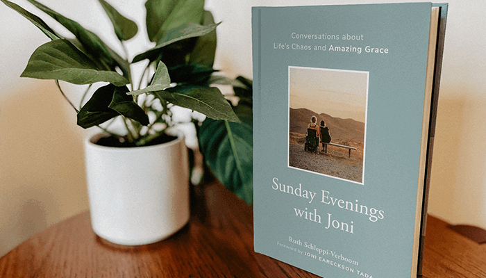 The book "Sunday Evenings with Joni" placed on a wooden table next to a small potted plant.