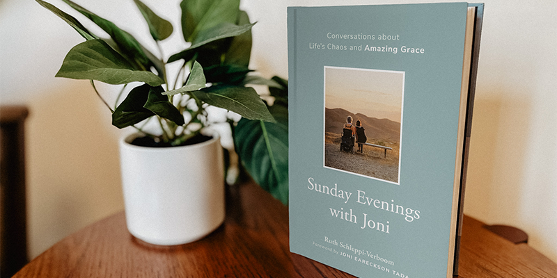 The book "Sunday Evenings with Joni" placed on a wooden table next to a small potted plant.