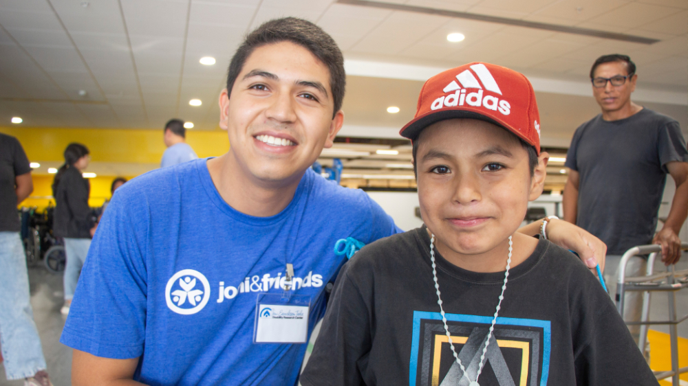 An intern in a blue Joni and Friends shirt and a boy in a red hat pose for a photo