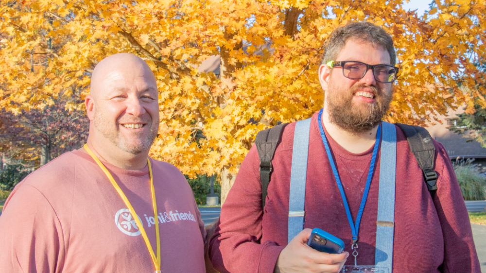 Two men pose for a photo in front of fall trees