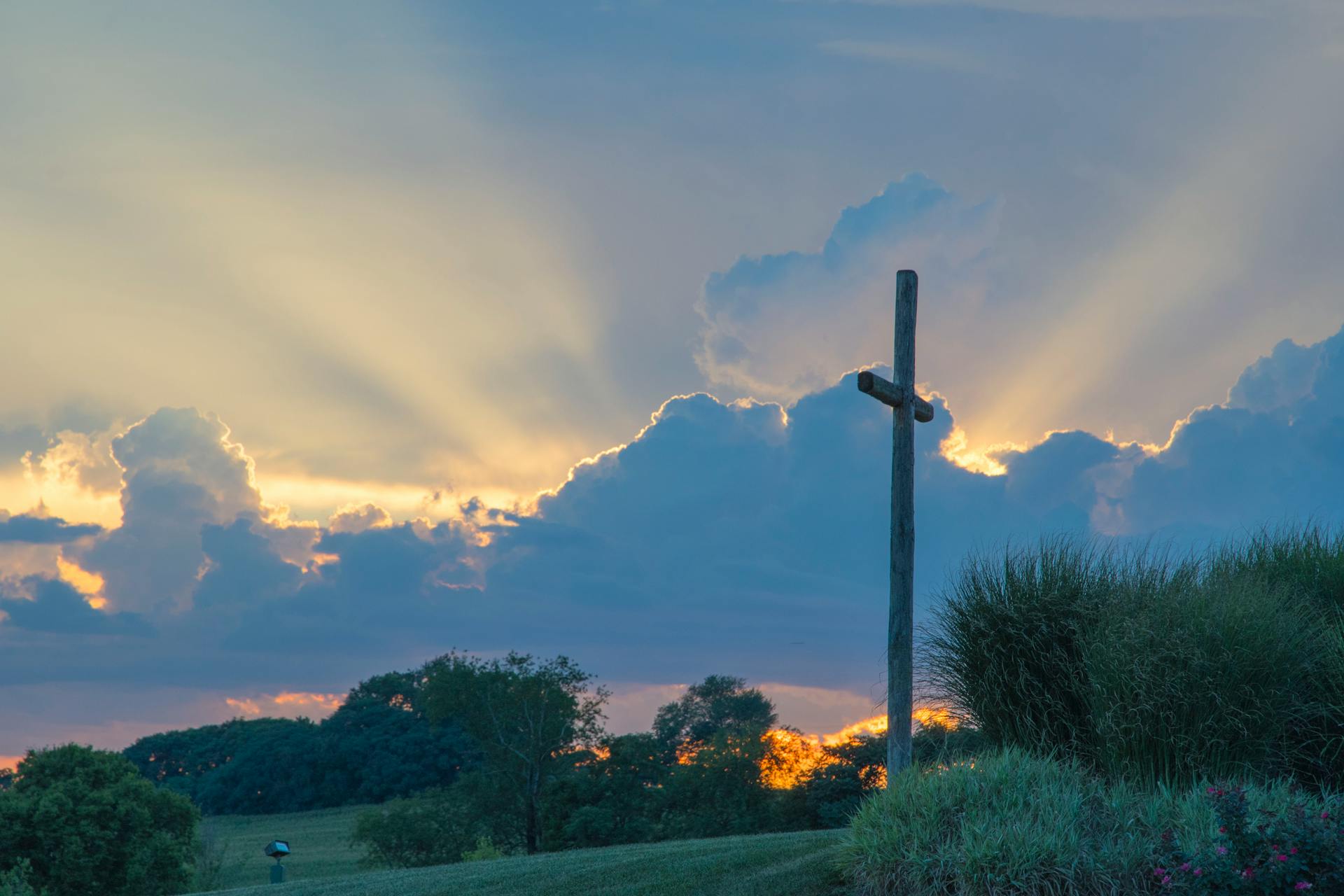 A cross silhouetted against a cloudy sky during sunrise.