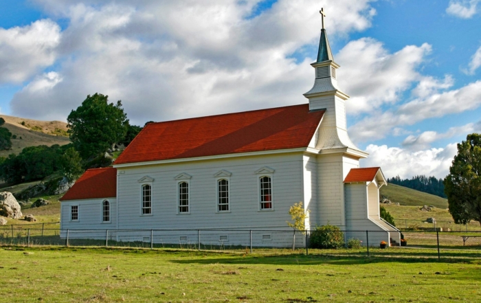 A rural church surrounded by a wide green field under an open sky.