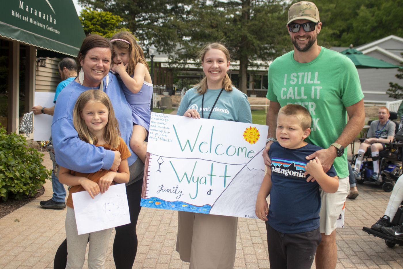 Austin and Melissa with their three children and a volunteer at Joni and Friends, holding a “Welcome Wyatt Family” cardboard sign.