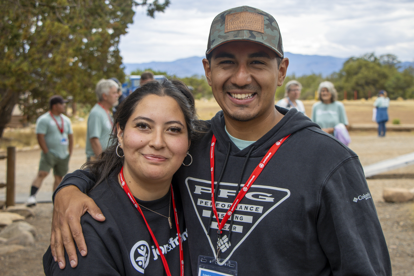 Alexus and Jaime smiling for the camera at an outdoor gathering, with other people mingling in the background.