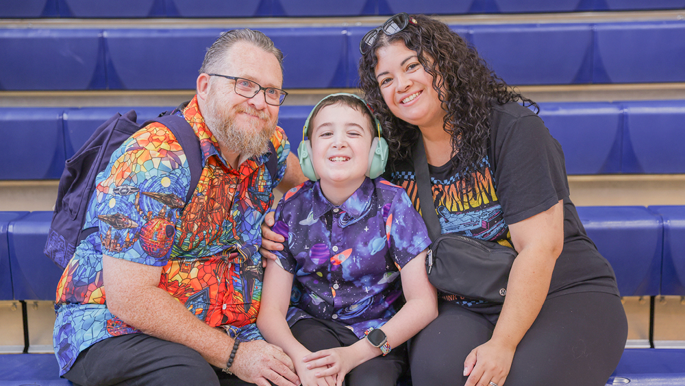 Mom, dad, and son with a disability sit together and smile at the camera.