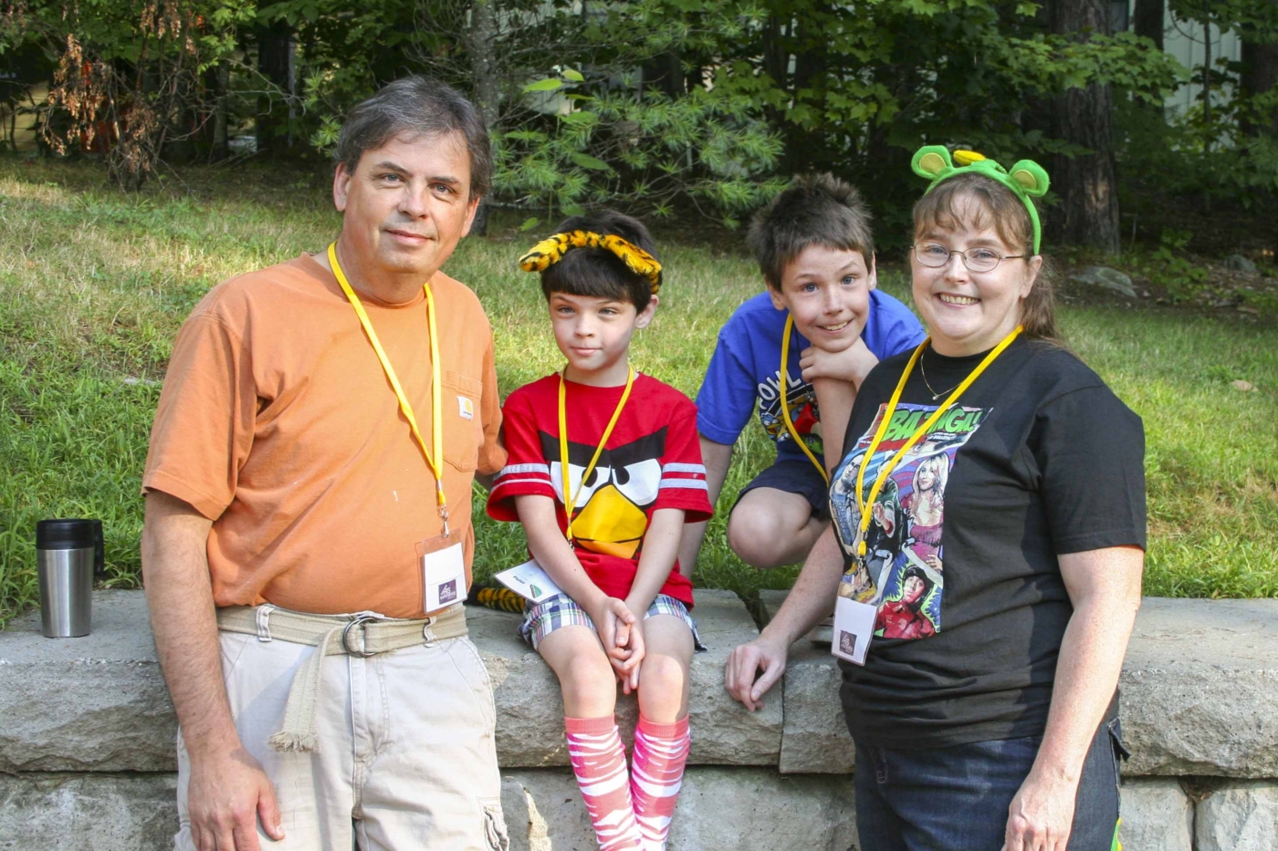 Jim and Annie with their two young sons posing for the camera with green grass and trees behind them.