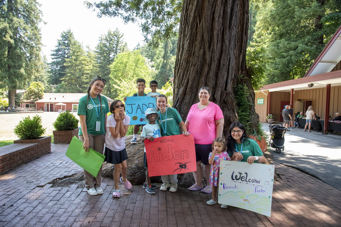 Natalie, a single mother, stands with her four children Aiden, Kylie, Jaden, and Hannah and their buddies at a Family Retreat, posing in front of a large tree trunk.