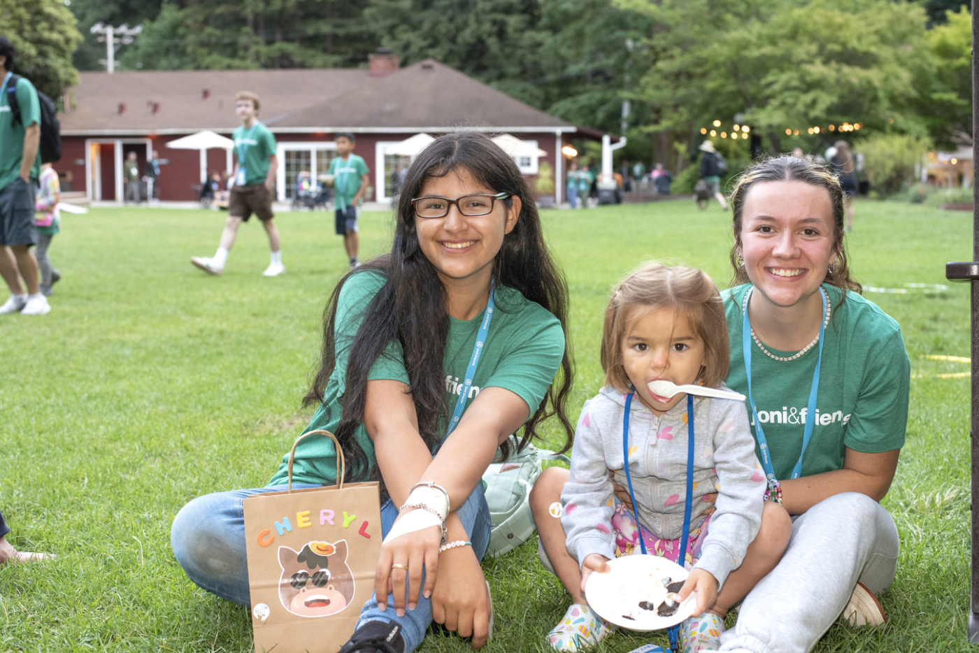 Hannah holds a plate of chocolates and has a spoon in her mouth while sitting on the grass next to her two buddies.