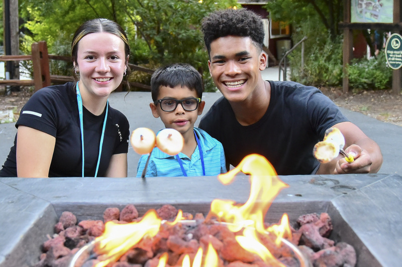Jaden is roasting marshmallows with a young boy and a woman during Family Retreat.