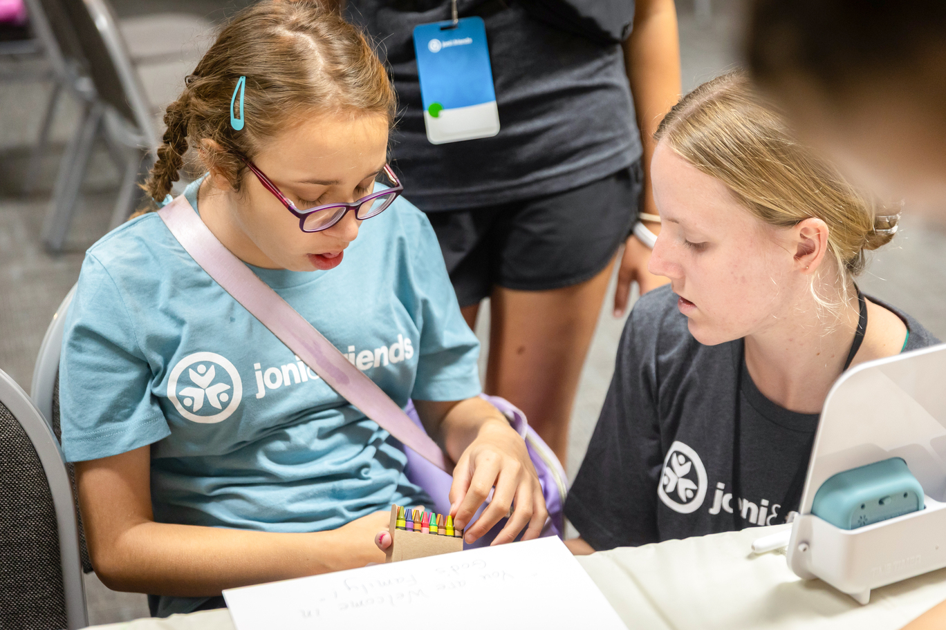 Lindsey pulls a crayon from a crayon box while sitting next to her buddy at Family Retreat.