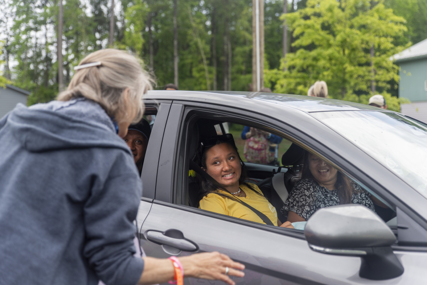 Sana sits in the car with her mother and father, the window down, being greeted by a volunteer at the Family Retreat.
