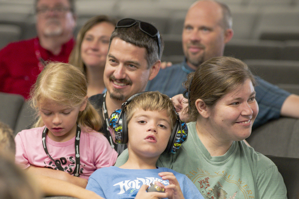 Jeremy, Crystal, Kaylee, and William seated and listening during a Family Retreat, with several other attendees visible in the background.