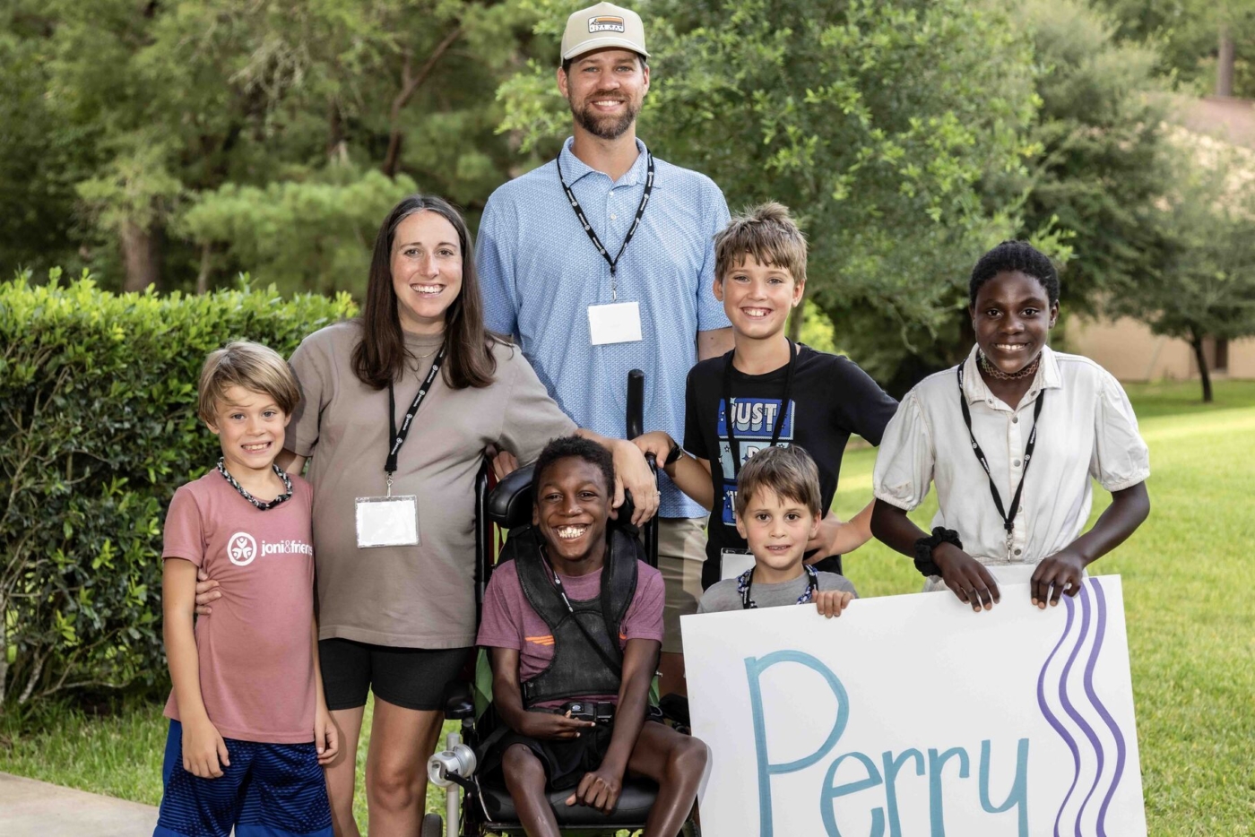 A family photo of Elyse and Kevin with their five children. Two of their sons are holding a piece of cardboard with the word “Perry” written on it as they all pose for the camera.
