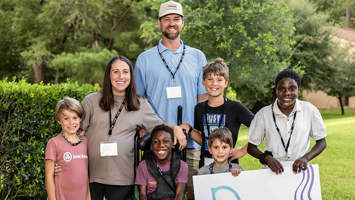 A family photo of Elyse and Kevin with their five children. Two of their sons are holding a piece of cardboard with the word “Perry” written on it as they all pose for the camera.