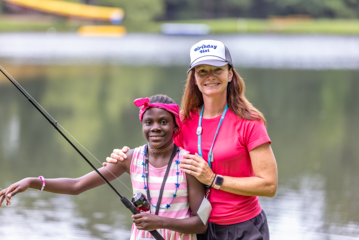 A girl holding a fishing rod looks at the camera while a woman beside her also poses. Both are smiling.