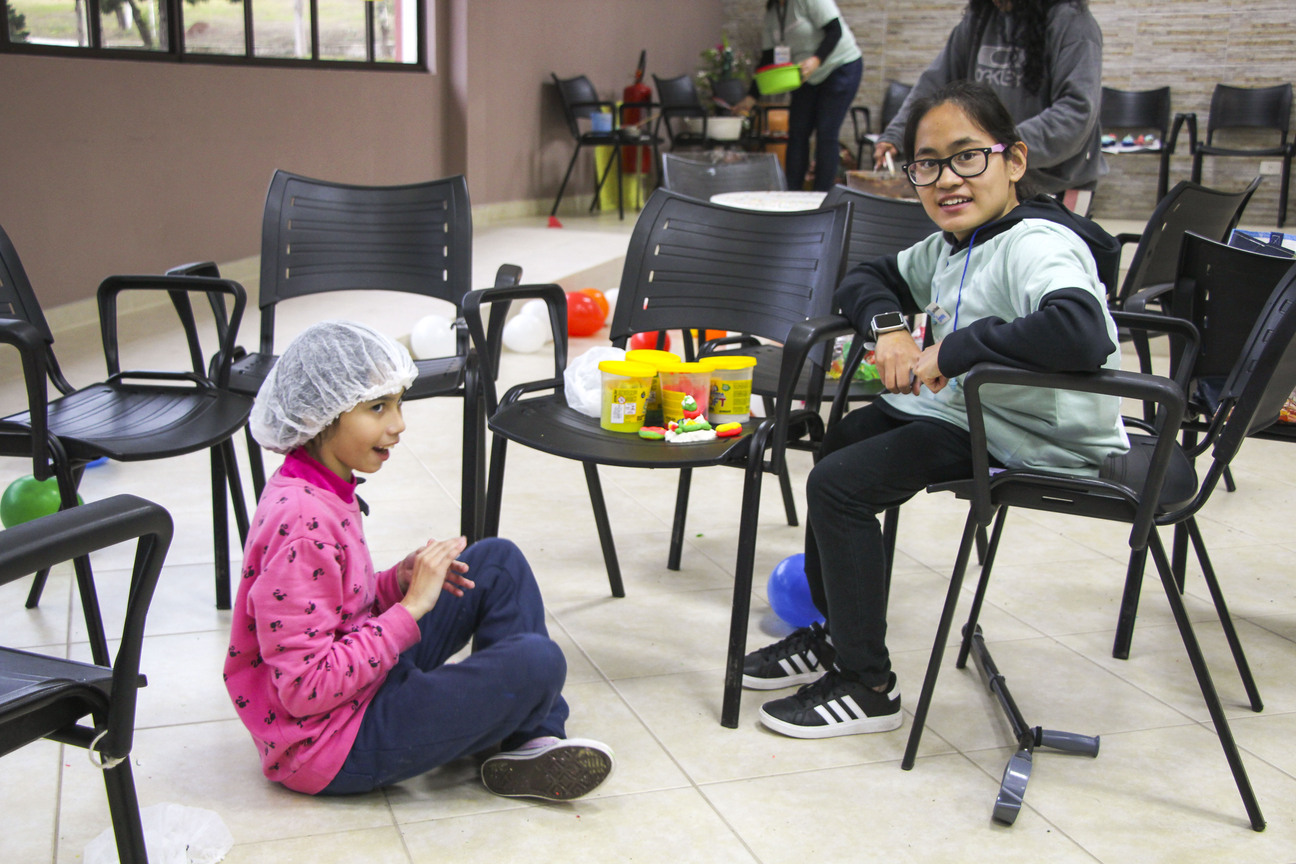Emma sitting on a chair while a little girl sits on the floor playing with clay.